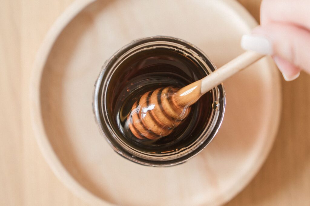 Wooden honey dipper resting in a jar of golden honey